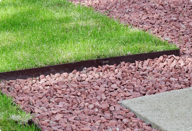 Corten steel garden edging bordering green lawn and red gravel garden bed