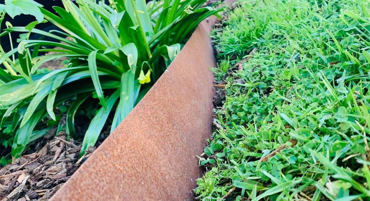 Close-up of rusty corten steel garden edging between lawn and garden bed